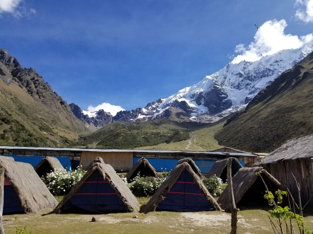 Refugios (chozas o carpas en base a ichu) en el campamento base de la ruta a la Laguna Humantay, con un nevado imponente en la Cordillera de Vilcabamba al fondo.