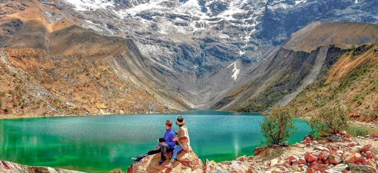Pareja de turistas en el mirador observando las tranquilas y turquesas aguas de la Laguna Humantay, ubicada a los pies de la montaña y el glaciar, en Cusco.