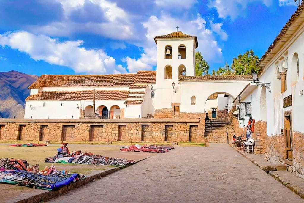 Vista del Monasterio y la Iglesia colonial de Chinchero, con artesanas vendiendo coloridos textiles en la explanada de la plaza inca.
