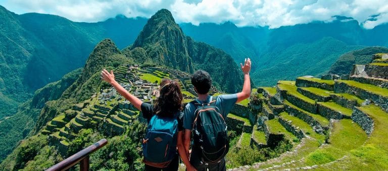 Pareja de turistas observan la extensión de la andenería (terrazas agrícolas) en la ciudadela inca de Machu Picchu, disfrutando de la vista panorámica del sitio arqueológico.