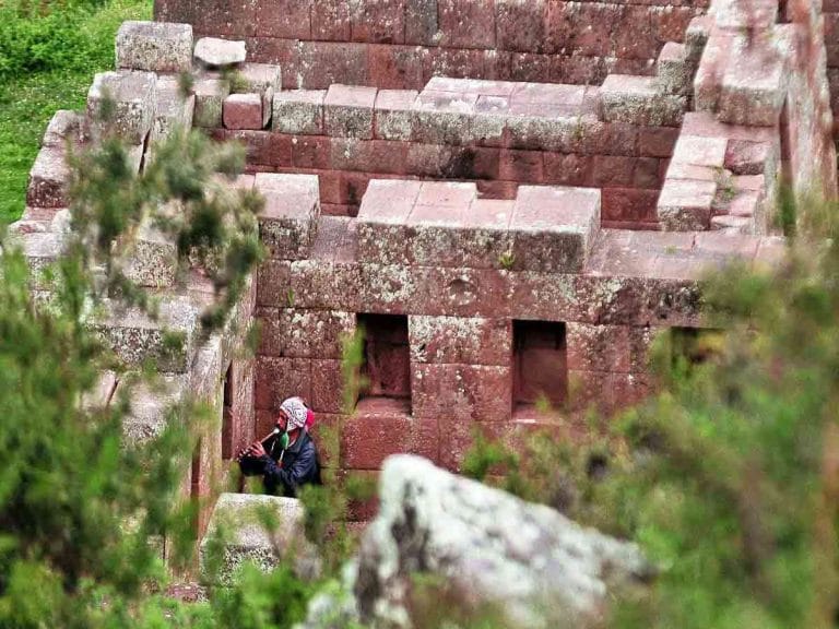 Muros de piedra inca y música tradicional en el Valle Sagrado: Un nativo toca un instrumento andino cerca de las construcciones ancestrales.
