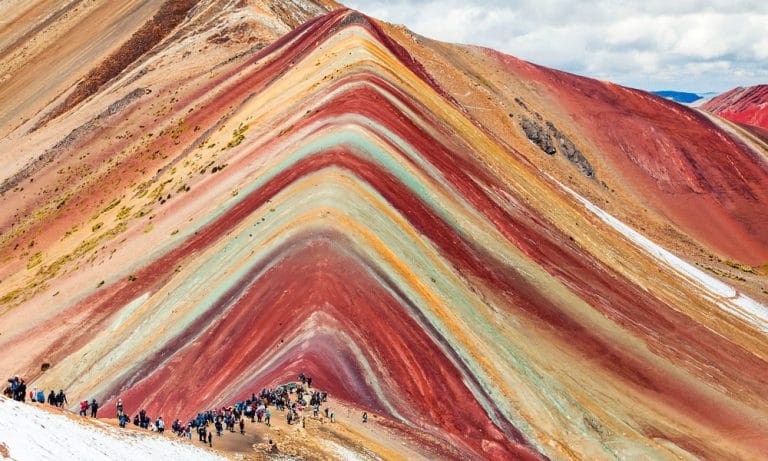 Decenas de turistas caminan por la ruta de senderismo en la alta montaña, dirigiéndose hacia la cima de la Montaña de Siete Colores (Vinicunca) en Cusco.