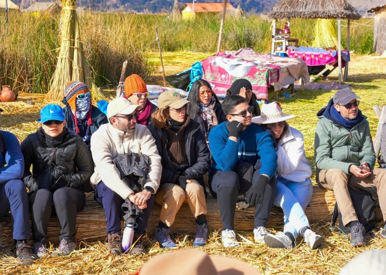 Turistas relajados y atentos escuchan la lección cultural Uros, sentados sobre la isla flotante de totora del Lago Titicaca.