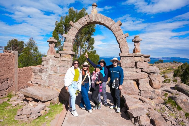 Portal de piedra en Taquile: Cinco turistas alegres posan en el arco de entrada tras subir los más de 550 escalones del puerto, Lago Titicaca.